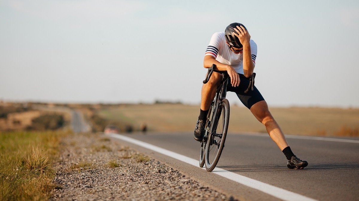 Cyclist bent over handlebars in exhaustion, illustrating foot numbness and discomfort from cycling